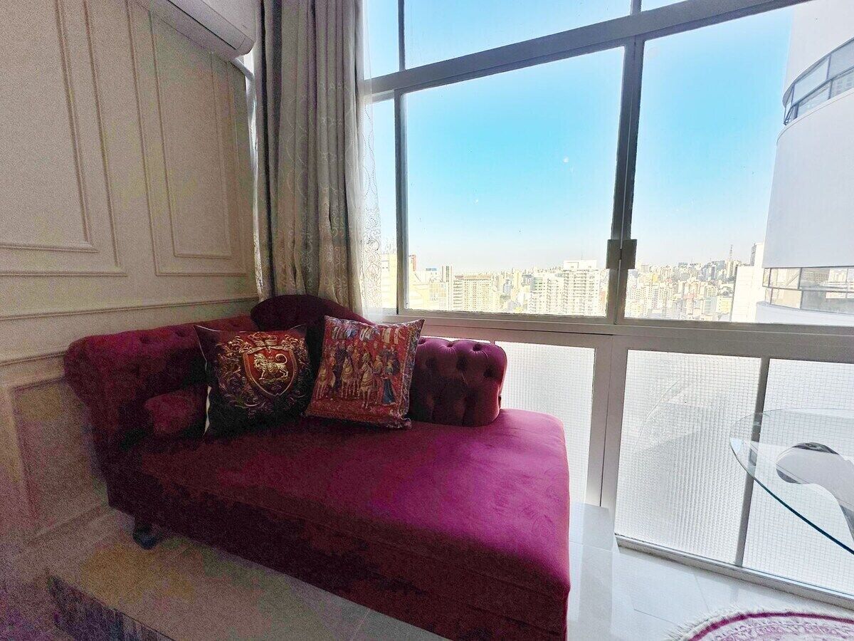 Ein Zimmer mit einem roten Samsofa, zwei Zierteichen und Blick auf eine Stadtkulisse durch große Fenster.