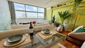 A dining area with a glass table, plates, wine glasses, and a bottle, set against a city view. - 2815M (São Paulo)