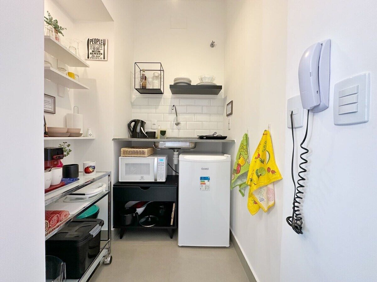 Une cuisine compacte avec des meubles blancs, un four à micro-ondes, un petit réfrigérateur et un téléphone fixé au mur.