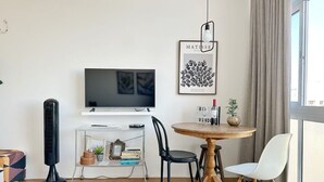 Een moderne woonkamer met een flatscreen televisie, een verticale ventilator, een ronde houten tafel met stoelen en een boekenkast.