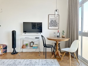 A modern living room with a flat-screen TV, a standing fan, a round wooden table with chairs, and a bookshelf. - 2011B (São Paulo)