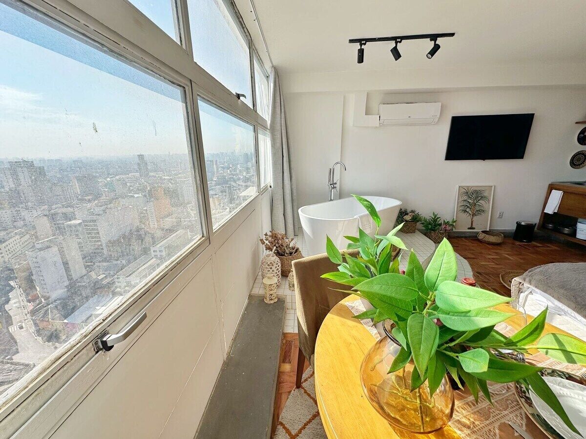 Een hoog appartementencomplex met uitzicht op de stad, een flatscreentelevisie, een witte badkuip en een eethoek met tafel en stoelen.