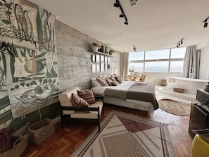 Ein Schlafzimmer mit einem großen Bett, einem Sofa, einem Wandbild und Blick auf die Stadt.