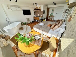 Ein Schlafzimmer mit Bett, großem Fenster und einem Badezimmer mit Badewanne.
