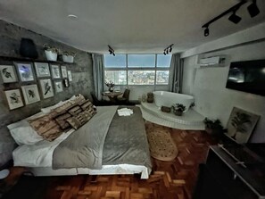 Ein Schlafzimmer mit einem großen Bett, einer Badewanne und Blick auf die Stadt.