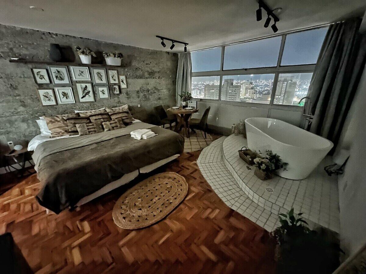 A bedroom with a large bed, a bathtub, and a city view.