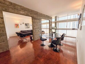 Uma sala de estar moderna com área de jantar, com uma janela grande, um sofá e uma mesa de vidro com cadeiras.