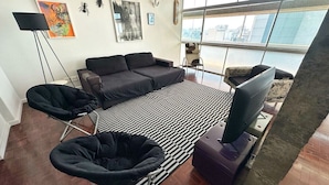 Uma sala de estar moderna com um conjunto de sofás, um tapete listrado em preto e branco e vista para a cidade através de grandes janelas.