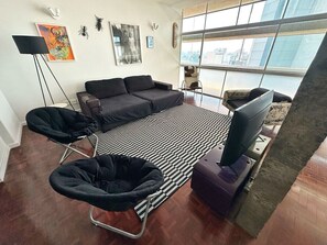 Ein modernes Wohnzimmer mit einer Sofagarnitur, einem schwarz-weißen Streifen Teppich und Blick auf die Stadt durch große Fenster.