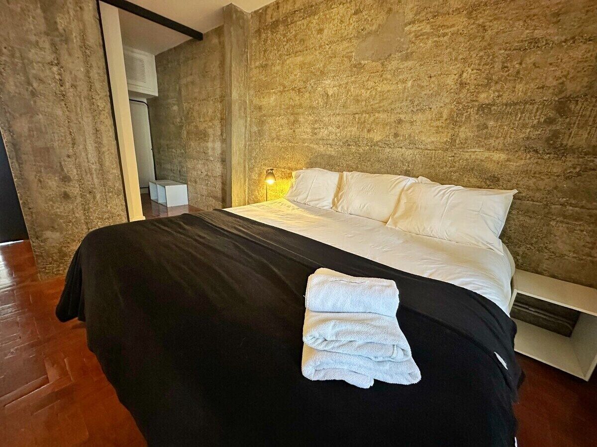 A modern bedroom with a large bed, a bedside lamp, and a wooden floor.