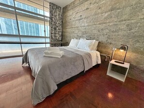 A bedroom with a large bed, a nightstand with a lamp, and a view through a window. - 0131C (São Paulo)