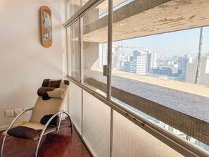 Une pièce offrant une vue sur le paysage urbain grâce à de grandes fenêtres, une chaise au design original et une œuvre d’art accrochée au mur.