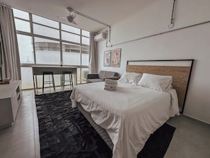 A modern hotel room with a large bed, a desk, and a view of the city through large windows. - 3213B (São Paulo)