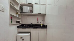 Eine kompakte Küche mit weißen Schränken, einer schwarzen Arbeitsplatte, einer Mikrowelle und einem kleinen Kühlschrank.