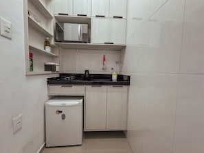 A compact kitchen with white cabinets, a black countertop, a microwave, and a small refrigerator. - 3213B (São Paulo)
