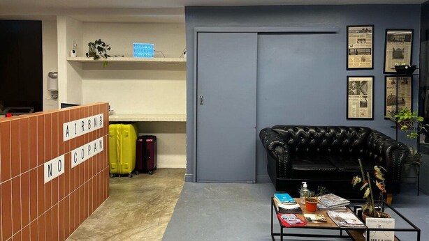 En hotellobby med en receptionsdisk, en sort lædersofa, et sofabord og et par potteplanter.