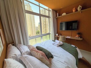 Habitación de hotel con una cama grande, un televisor en la pared y vistas de edificios altos.