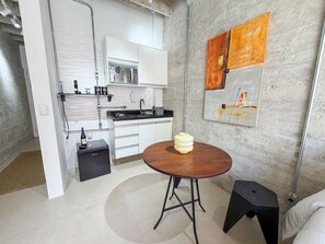 A modern kitchen with white cabinets, a round wooden table, and a black stool. - 0202B (São Paulo)