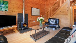 Ein gemütliches Holzhaus-Interieur mit Kamin, einer Couch, einem Couchtisch und einem Fernseher.