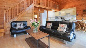 Ein gemütliches Cabin-Interieur mit einer Holztreppe, einem Wohnbereich mit Ledersofas, einem Holzesstisch und einer Küche mit weißen Schränken.