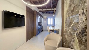 Une cuisine moderne dotée d’un four encastré, d’un coin repas avec une table en marbre et d’un téléviseur fixé au mur.