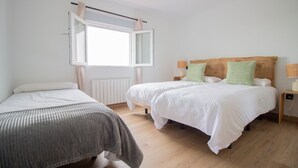 Un dormitorio con dos camas, una ventana con cortinas, un radiador y suelo de madera.