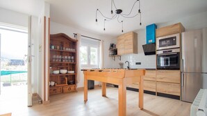 Una cocina moderna con armarios de madera, mesa de fútbol y vista a través de un ventanal abierto.
