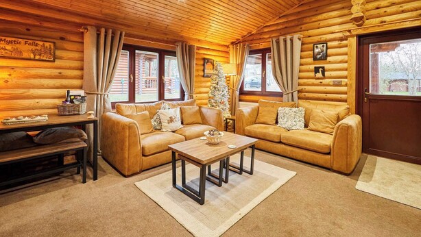 A log cabin interior with two leather sofas, a wooden coffee table, and a Christmas tree.
