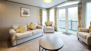 A living room with a beige sofa, two armchairs, a round coffee table, and a large window with curtains.