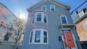 A two-story building with a corner bay window, a red door, and a small front porch with steps. - Spacious & sunny 4-bedroom home in the heart of Portland's charming West End (Portland)
