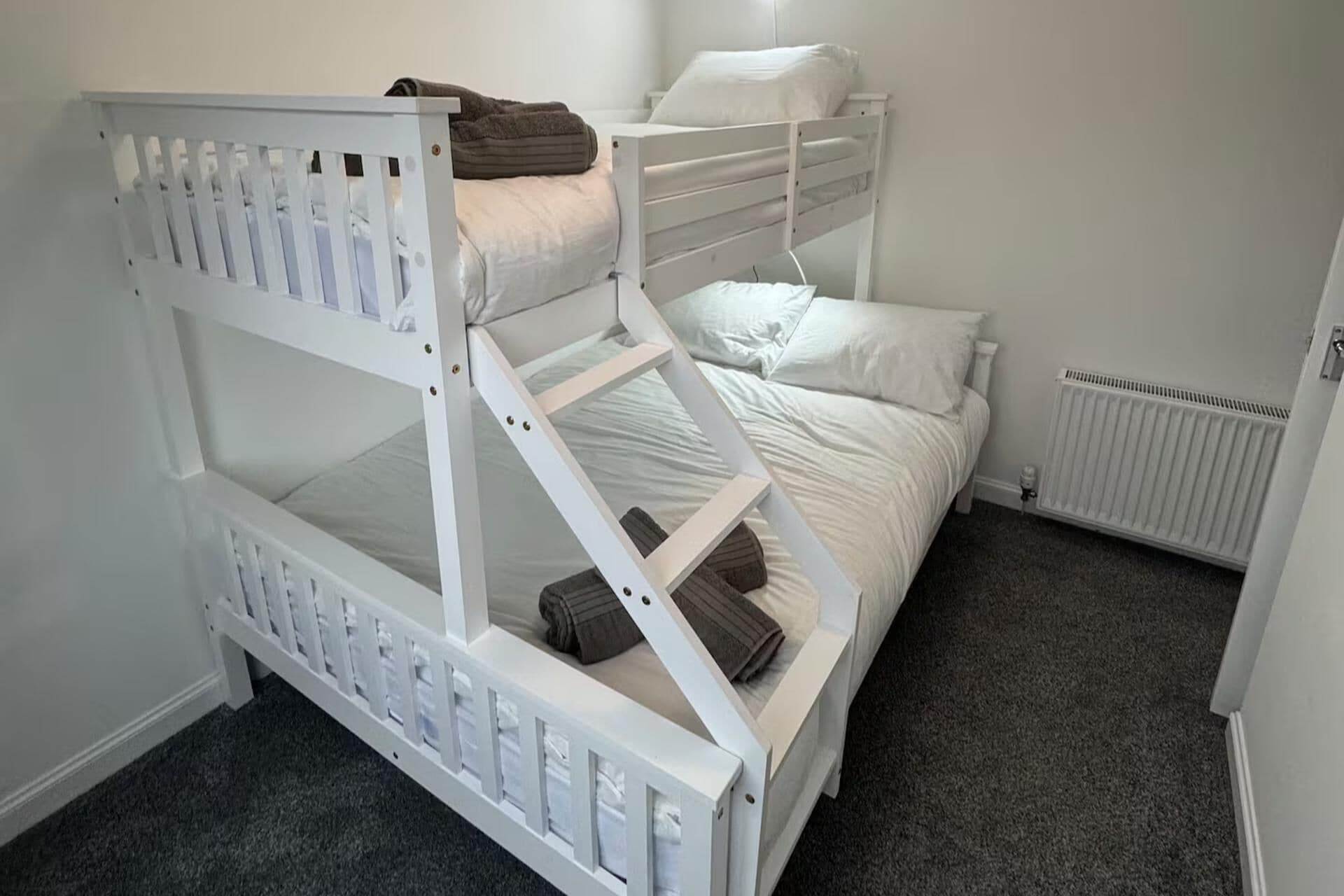 Uma cama beliche com estrutura branca e carpete cinza.