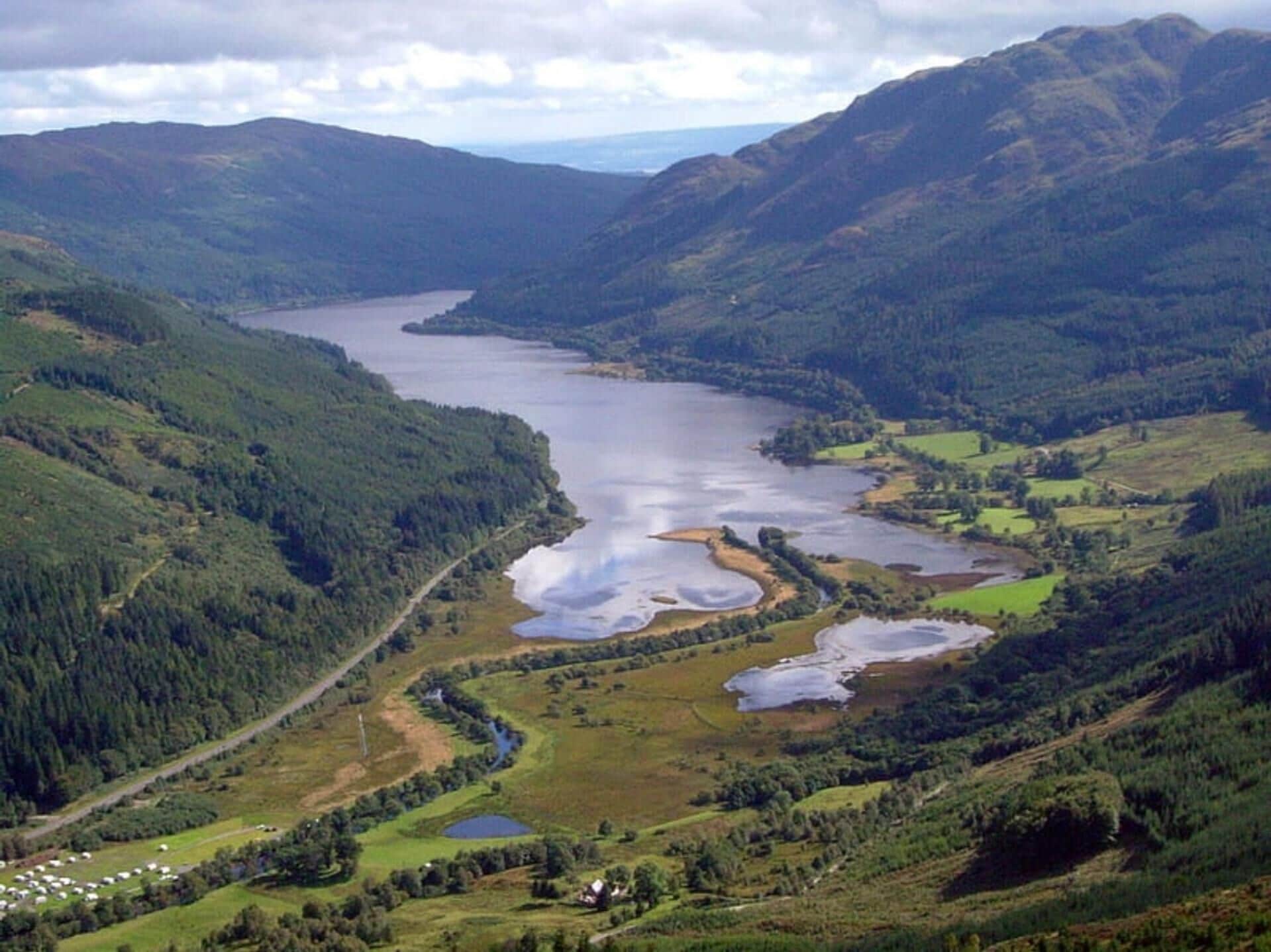 A mountainous landscape with a lake, surrounded by dense forests and small ponds.