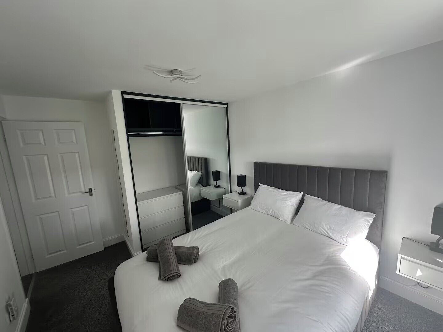 A hotel room with a large bed, a bedside table with a lamp, a mirror, and a wardrobe.