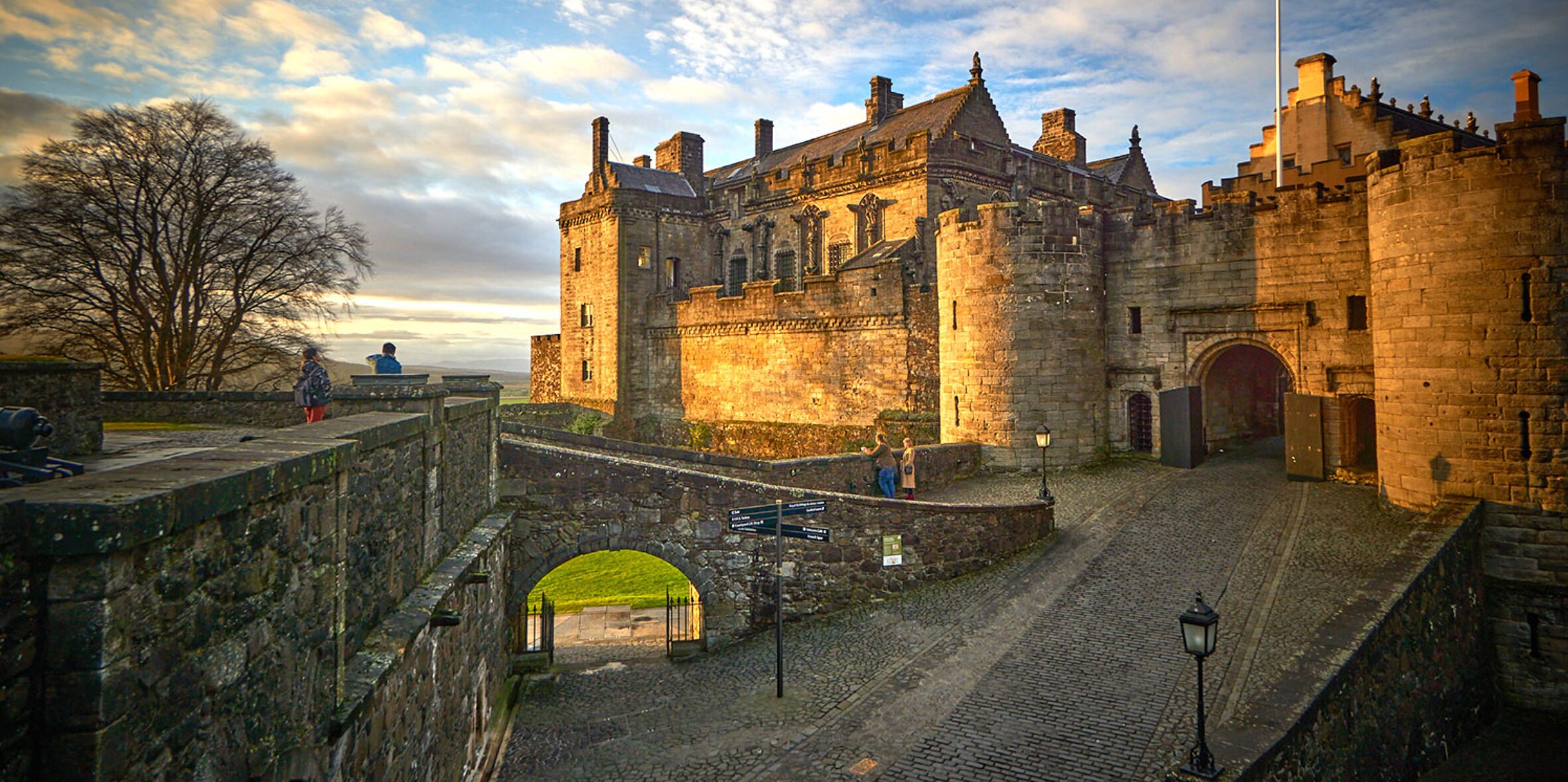 A historic stone castle with a cobblestone courtyard, a bridge, and a view of the surrounding landscape.