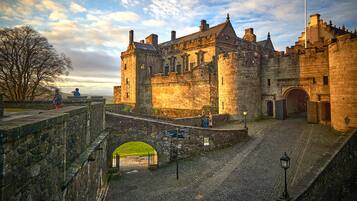 A historic stone castle with a cobblestone courtyard, a bridge, and a view of the surrounding landscape.