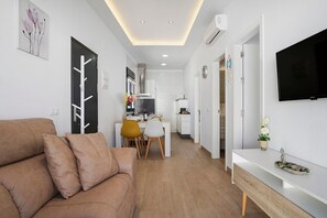 Uma sala moderna com sofá, área de jantar com cadeiras, cozinha com armários e televisão na parede.