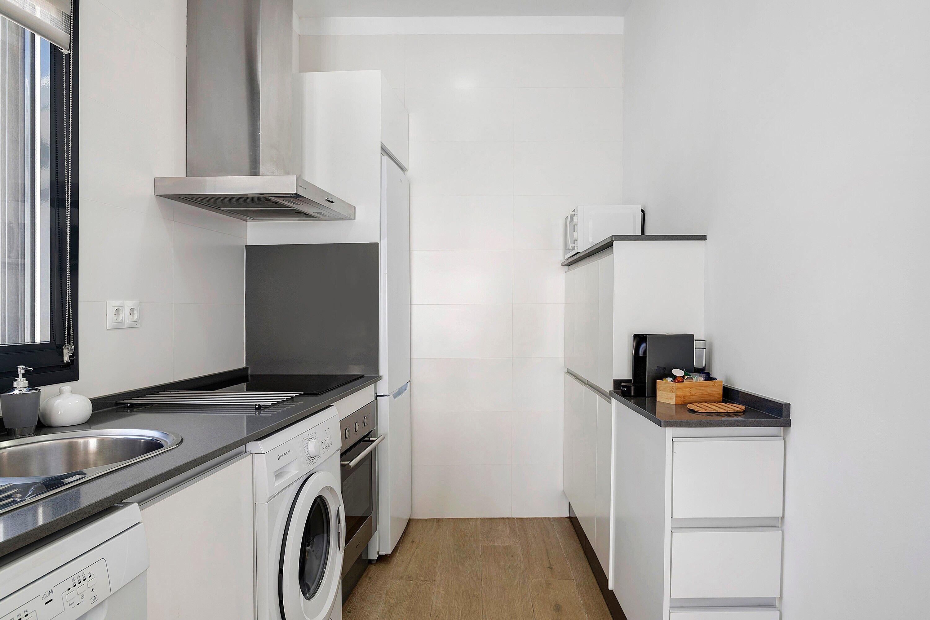 A compact kitchen with a washing machine, a built-in oven, a stainless steel sink, and a microwave.