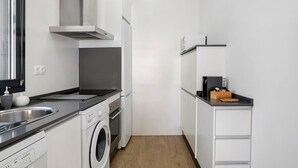 Ett kompakt kök med tvättmaskin, inbyggd ugn, diskho i rostfritt stål och mikrovågsugn.