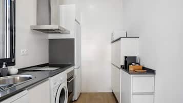 A compact kitchen with a washing machine, a built-in oven, a stainless steel sink, and a microwave.