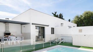 Ett modernt hus med en swimmingpool, en uteplats och ett område för grillning.