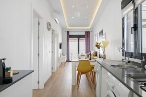 Een moderne keuken met een geïntegreerde vaatwasser, een eethoek met een gele stoel, en uitzicht op de woonkamer.