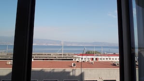 A view from a window overlooking a coastal area with a bridge, a red-roofed building, and distant mountains. - Central Palace (Reggio Calabria)