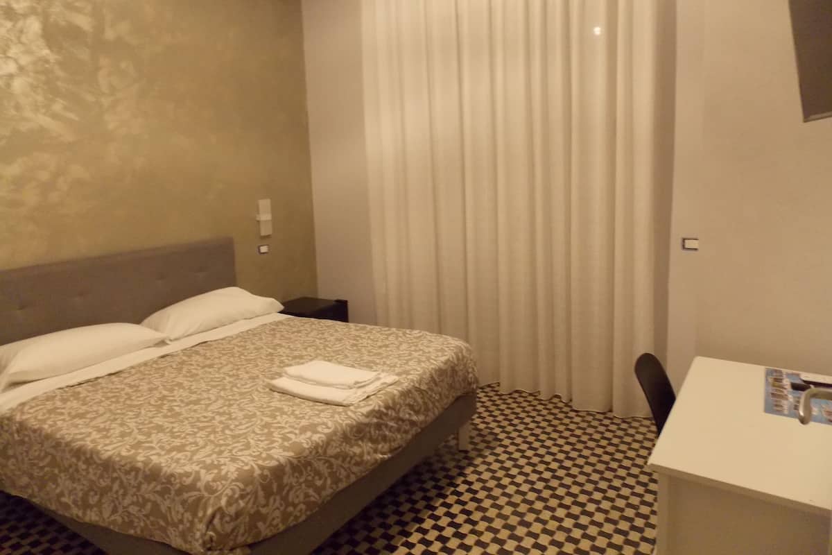 A hotel room with a bed, a desk, a chair, and a checkered floor.