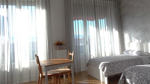 A bedroom with two beds, a wooden table with chairs, and a window with sheer curtains. - Central Palace (Reggio Calabria)