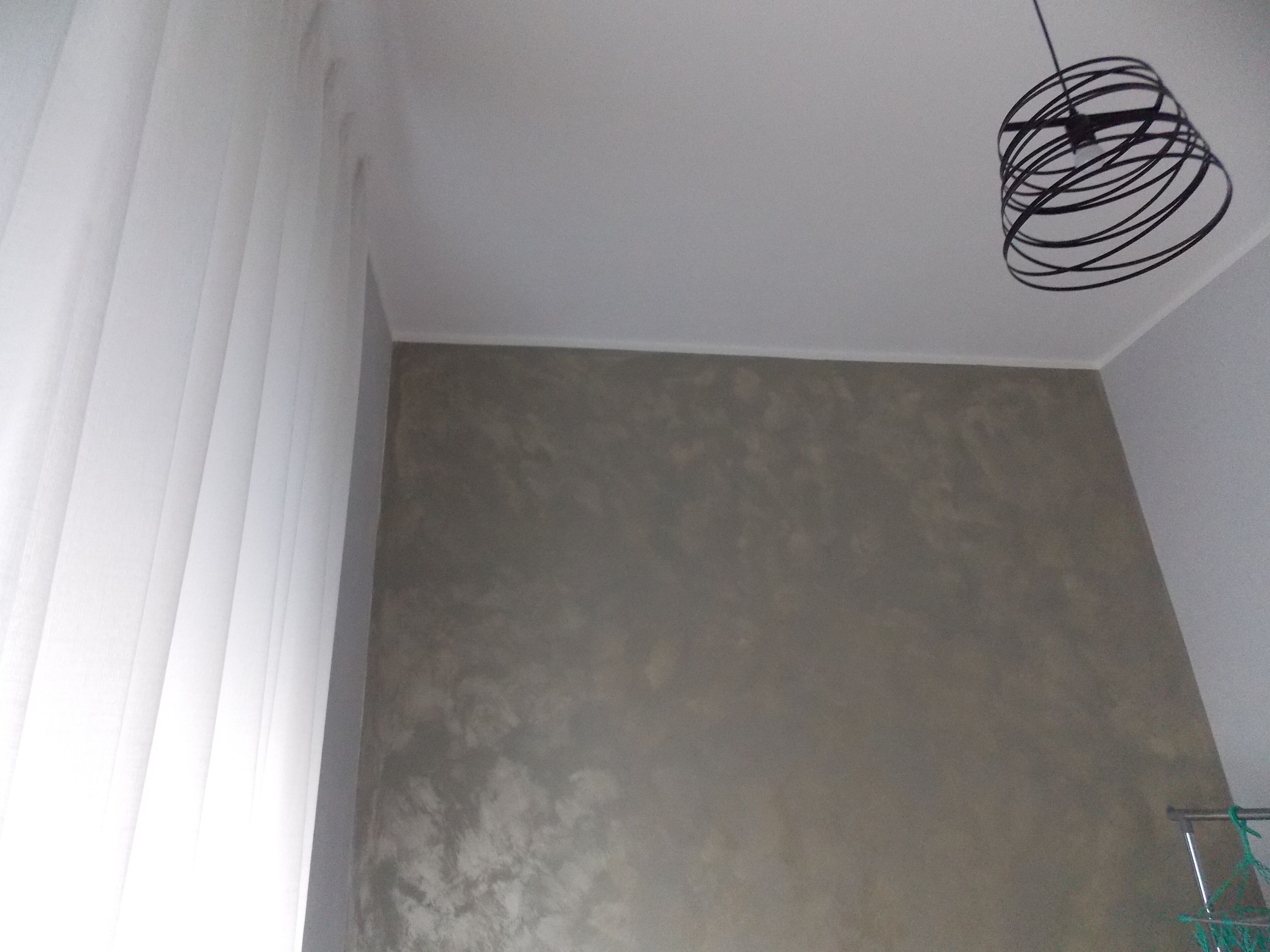 A room with a plain wall, a hanging light fixture, and a window with blinds.