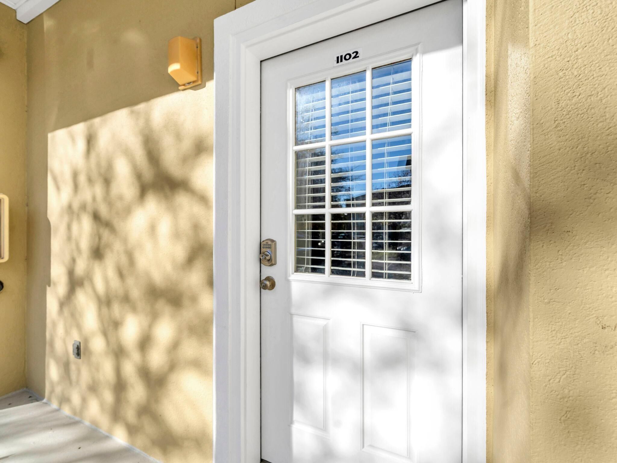 A white door with a window and a number plate, set in a beige wall.