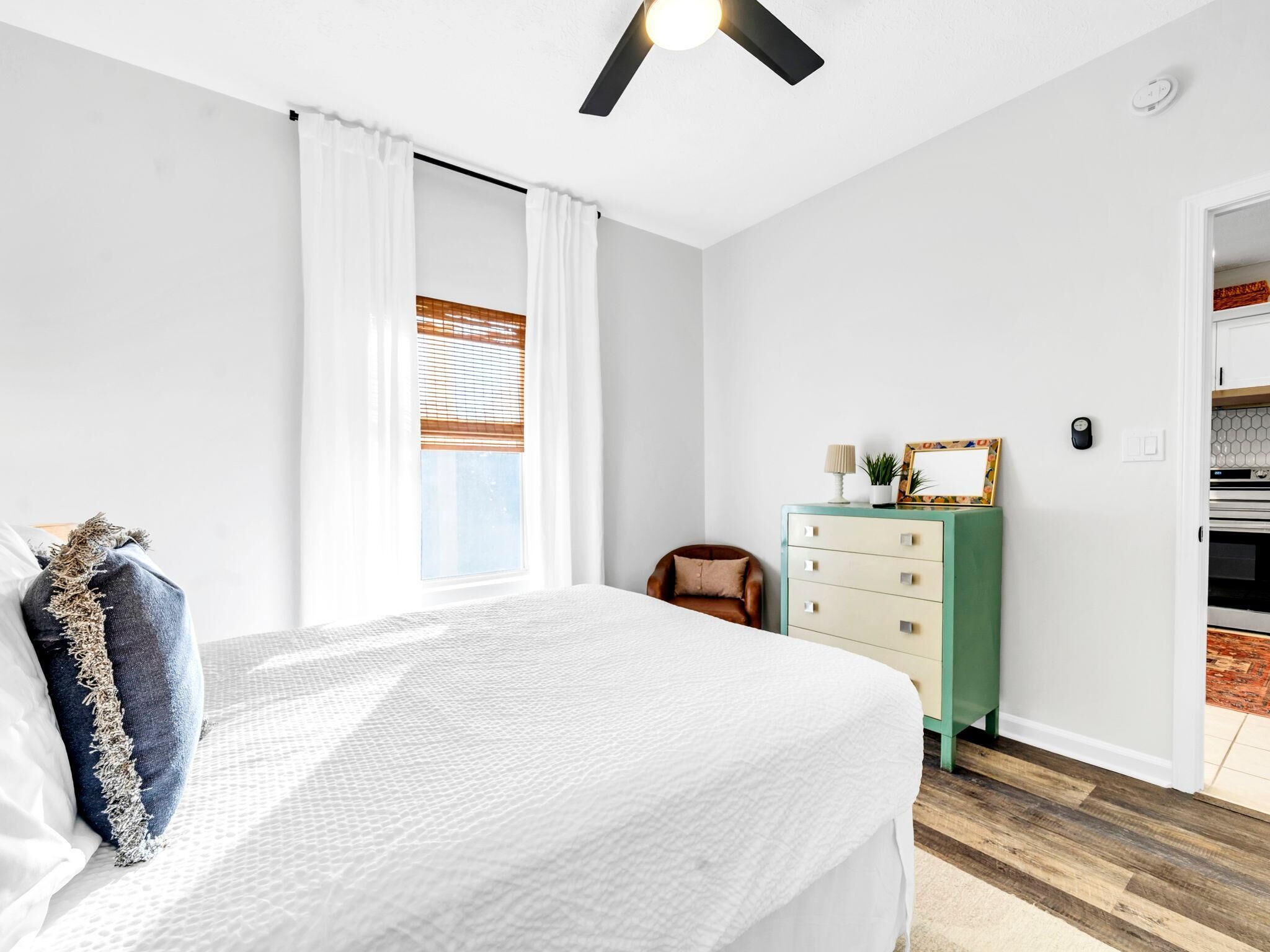 A bedroom with a bed, a dresser, a chair, and a ceiling fan.