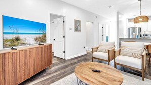 Ein modernes Wohnzimmer mit großem Fernseher, Holzmöbeln und Blick auf den Strand.