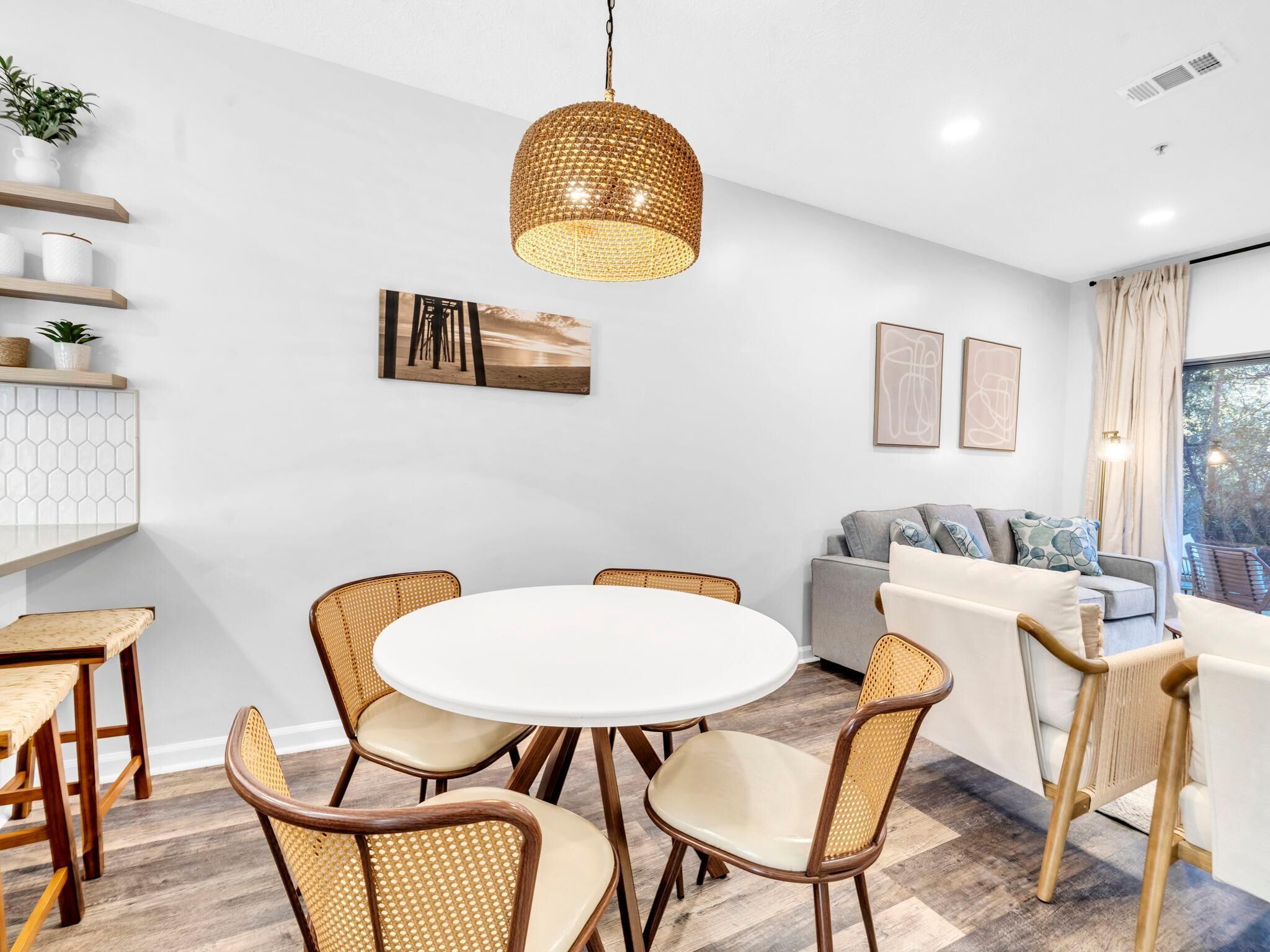 A modern dining area with a round table, wicker chairs, and a hanging light fixture.