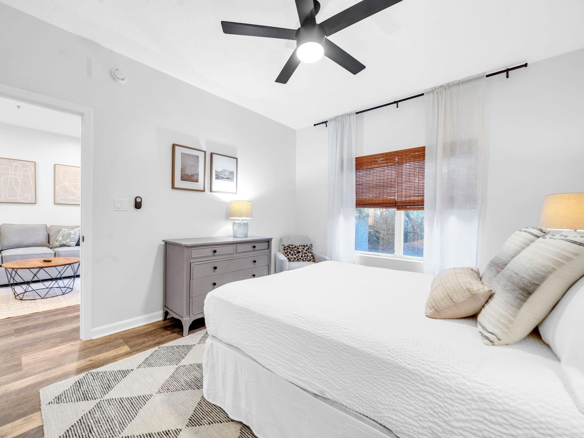 Ein Schlafzimmer mit Bett, Schreibtisch, Stuhl, Deckenventilator und einem Fenster mit Jalousien.